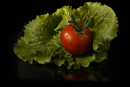 Red tomato fruit on green cabbage leaf on dark background.