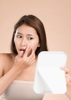 Portrait of young ardent asian woman looking in the mirror worry about pimple on her face. Beauty care for skin problem, acne treatment concept.