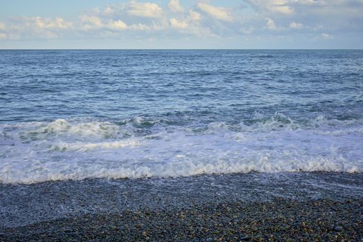 Sea shore with pebbles, wet sea pebbles on the beach and quiet sea surf. Restless sea and waves.