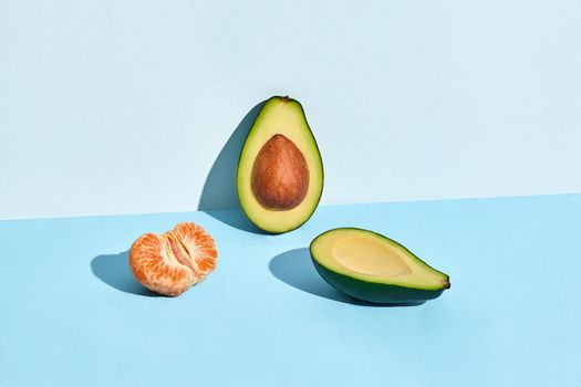 Composition of fresh fruits, half of peeled mandarin and two halfs of cutted avocado on blue background. Mock up, two-colored pastel