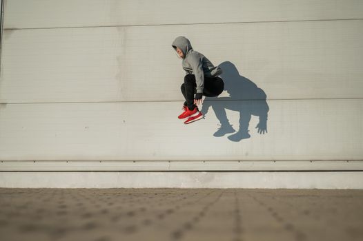 Caucasian man in hoodie jumping high with hands on knees outdoors