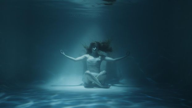 red-haired woman meditating underwater in white dress in 4k