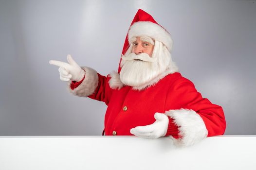 Santa Claus peeks out from behind an ad on a white background. Merry Christmas