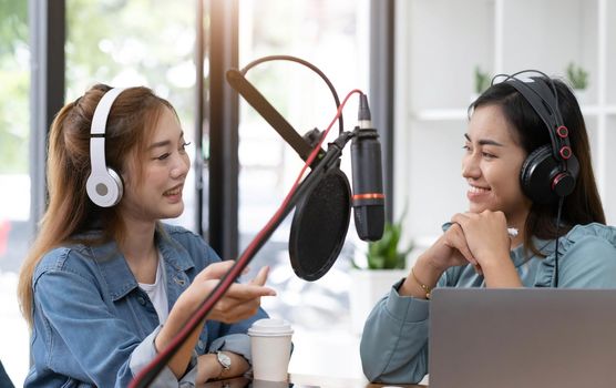 Smile two asian young woman, man radio hosts in headphones, microphone while talk, conversation, recording podcast in broadcasting at studio together. Technology of making record audio concept..