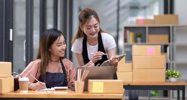 Portrait of Starting small businesses SME owners, two Asian woman check online orders Selling products working with boxs freelance work at home office, sme business online small medium enterprise.