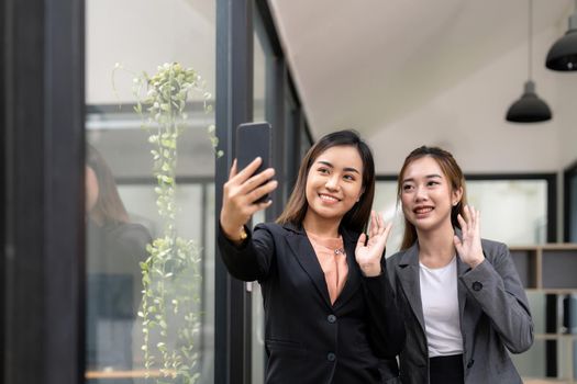 Two asian business woman waving hands to greeting partner during making video conference with her team