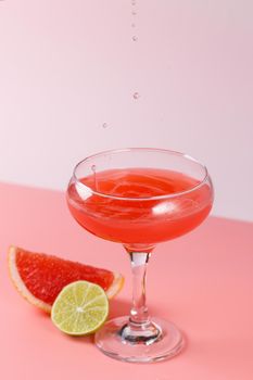 Fresh grapefruit juice with drops falling into a glass on a pink background with grapefruit slices and lime on a pink background. Copy space