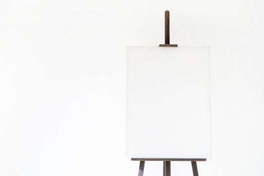 Wooden easel with blank canvas on light wall background for mockup design. Space for text