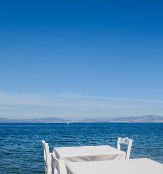 White restaurant tables on the beach in summer - travel, vacation and summer concept. The perfect lunch with a sea view