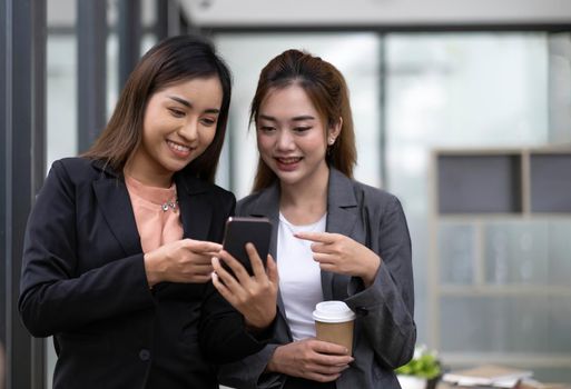 Two asian businesswoman in formal suit in office happy and cheerful during using smartphone and working in the office..