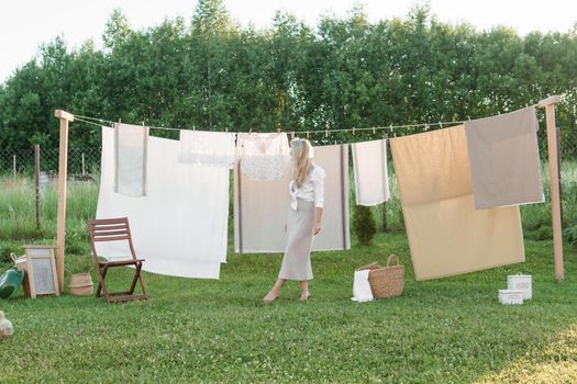 Laundry day. A woman hangs linen and towels on a tree in the courtyard of a village house. Summer cottage concept.