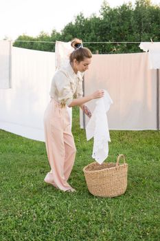 Laundry day. A woman hangs linen and towels on a tree in the courtyard of a village house. Summer cottage concept.