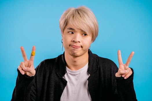 Asian man showing with hands and two fingers air quotes gesture, bend fingers isolated over blue background. Not funny, irony and sarcasm concept