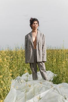 An Asian model poses in a field of yellow flowers for a clothing brand, polyethylene is the main props for a photo shoot. The concept of manufacturing clothing from recycled plastic. A woman in a pantsuit is standing on a plastic bag.