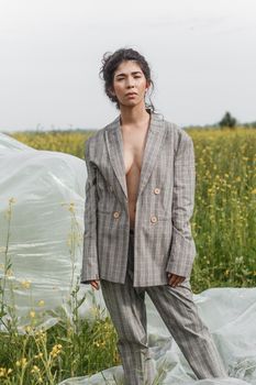 An Asian model poses in a field of yellow flowers for a clothing brand, polyethylene is the main props for a photo shoot. The concept of manufacturing clothing from recycled plastic. A woman in a pantsuit is standing on a plastic bag.