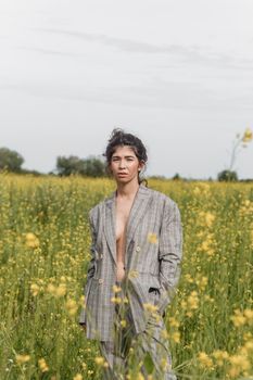 An Asian model poses in a field of yellow flowers for a clothing brand, polyethylene is the main props for a photo shoot. The concept of manufacturing clothing from recycled plastic. A woman in a pantsuit is standing on a plastic bag.