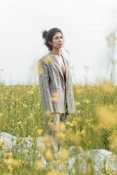 An Asian model poses in a field of yellow flowers for a clothing brand, polyethylene is the main props for a photo shoot. The concept of manufacturing clothing from recycled plastic. A woman in a pantsuit is standing on a plastic bag.