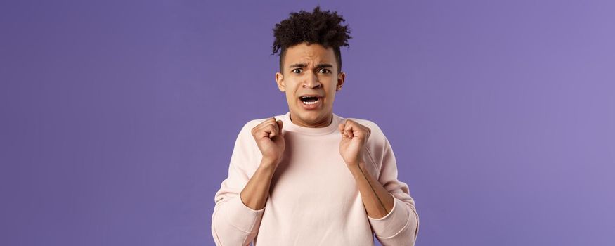 Close-up portrait of worried, anxious funny hispanic man jumping from fear, gasping look concerned, starting to panic before important meeting, standing purple background afraid and nervous.