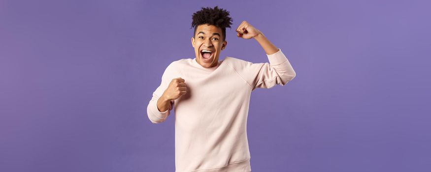 Portrait of excited happy man seeing his team scored goal on sports tv channel, chanting raise one hand in triumph, screaming in joy and happiness, celebrating victory, placed right bet.