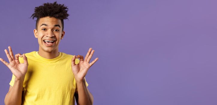 Close-up portrait of upbeat, relaxed young hipster guy with dreads assuring all good, everything be okay, show OK gesture and smiling, no problem guarantee best quality, purple background.