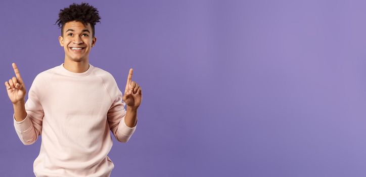 Waist-up portrait of dreamy, handsome 25s young hispanic man seeing good promotion, best deal or offer from online shop, pointing fingers top advertisement, looking up with satisfied smile.