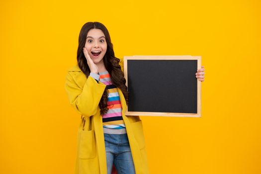 Teenage girl child holding blackboard, isolated on a yellow background. Amazed teenager. Excited teen girl