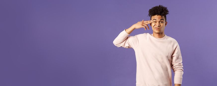 Portrait of young teenage guy, hispanic male student losing his mind at home lockdown, pointing at temple with finger gun and grimacing as shooting himself from boredom or annoyance.