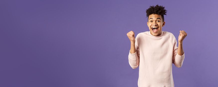 Portrait of happy, cheerful triumphing young hipster guy with dreads, dancing like champion, celebrating success or victory, passed test, fist pump smiling and rejoicing, purple background.