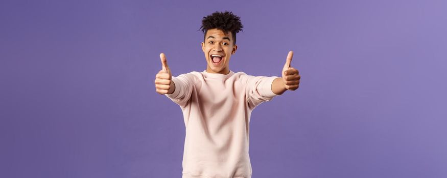 Portrait of satisfied young happy man think event was super cool, recommend use company service, assure in best quality, like and approve awesome product, standing purple background.