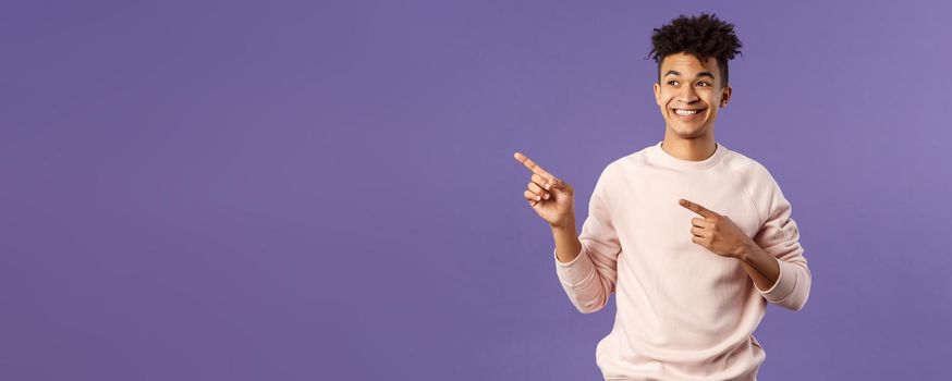 Portrait of enthusiastic, good-looking hispanic man with dreads, looking and pointing upper left corner with satisfied beaming smile, seeing cool thing, made his choice, purple background.