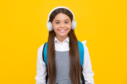 School girl in headphones on isolated studio background. School and music concept. Happy girl face, positive and smiling emotions