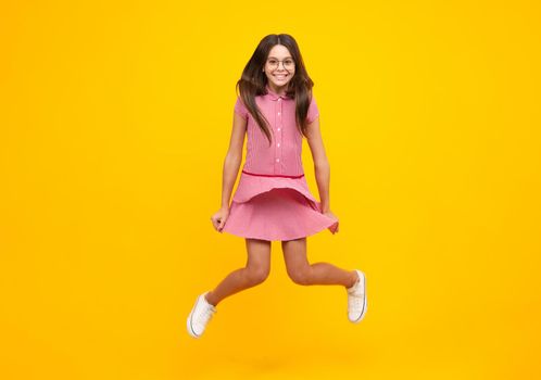 Full length cheerful teenager kid jump enjoy rejoice win isolated on yellow background. Small child girl in summer dress jumping