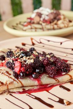 photo of delicious crepe with red berries, blackberries, blueberries, blueberries, strawberries and chocolate decoration. sweet crepe.