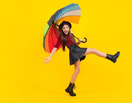 Fashion autumn kids weather. Child teenager girl with umbrella in autumn black leather skirt boots and hat isolated on yellow studio background. Excited teenager, glad amazed and overjoyed emotions