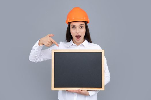 Young woman in helmet hold board on gray background. Architect businesswoman in helmet thinking, young caucasian female in work as constructor engineer. Funny emoticons girl in a construction helmet