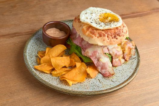 photo of delicious bacon burger accompanied with an egg, chipotle dressing and dehydrated bananas on wooden table. big hamburguer.