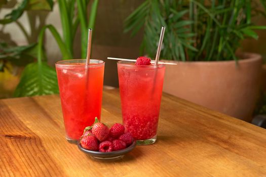 tropical red fruit drink on wooden table with plant background. strawberries, raspberries, red color drink