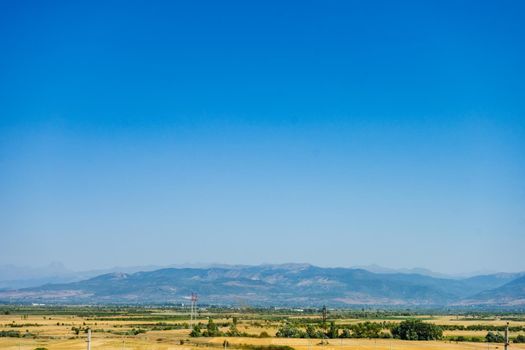 Summer landscape of central Georgia with harvested wheat field and Caucasus mountain