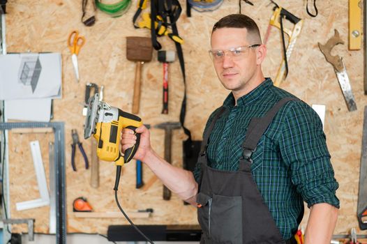 Portrait of a man with an electric jigsaw on wood in the workshop