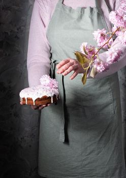 a woman decorates a homemade Easter cake with pink sakura flowers, spring blossom, a bouquet of pink sakura flowers on a table in a decorated spring room, a beautiful still life. High quality photo