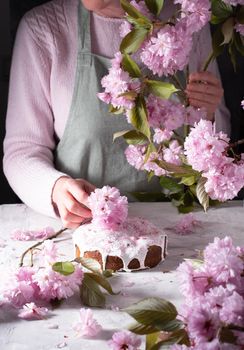 a woman decorates a homemade Easter cake with pink sakura flowers, spring blossom, a bouquet of pink sakura flowers on a table in a decorated spring room, a beautiful still life. High quality photo