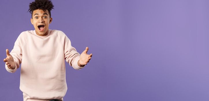 Portrait of surprised happy young man reaching hands to hug friend seeing him on street, rejoicing over big great news, standing impressed and thrilled over purple background.