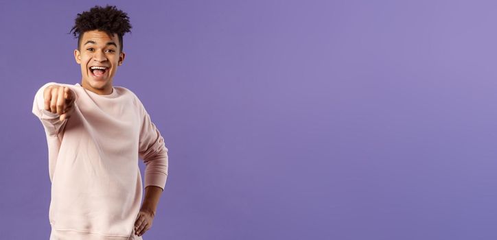 Portrait of outgoing happy hispanic male student making his choice, laughing over something extremely funny point finger at camera with amused smile, standing purple background.