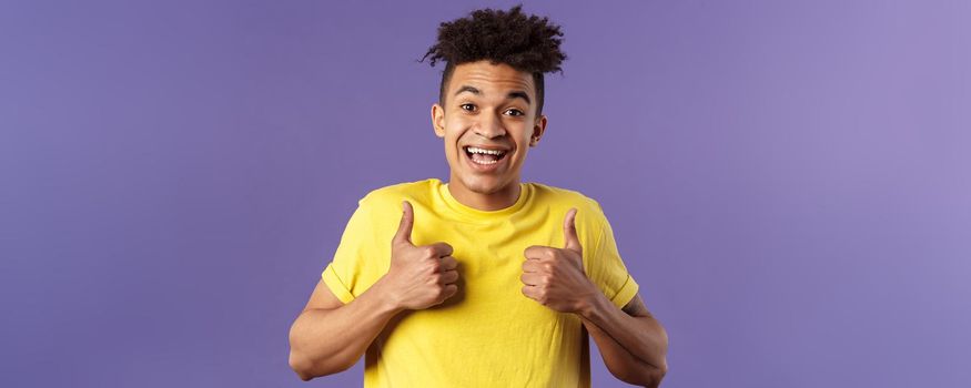 Close-up portrait of enthusiastic healthy hispanic guy staying positive, show thumbs-up and smiling, encourage people stay home, feel fine, like and approve friends plan, standing purple background.
