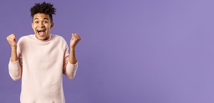 Portrait of happy, cheerful triumphing young hipster guy with dreads, dancing like champion, celebrating success or victory, passed test, fist pump smiling and rejoicing, purple background.