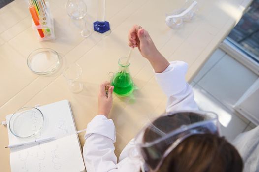 Schoolchild holding a test tube and dripping a few drops of a chemical solution while doing experiments in a chemistry lesson in a school science lab. Open to new knowledge in new academic year