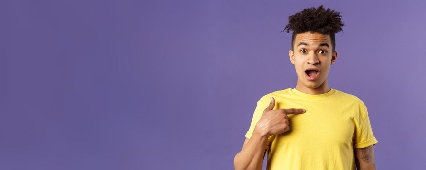 Who me, no way. Portrait of surprised, happy rejoicing young man looking with disbelies as being chosen from all candidates, pointing at himself open mouth fascinated, purple background.