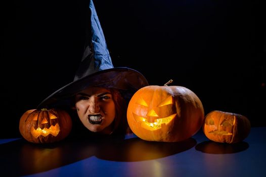 The head of an evil witch is on the table next to the glowing pumpkin jack-o-lantern.