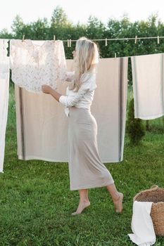 Laundry day. A woman hangs linen and towels on a tree in the courtyard of a village house. Summer cottage concept.