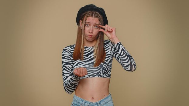 Need some more, please give me. Lovely young woman showing a little bit gesture with sceptic smile, showing minimum sign, measuring small size. Adult stylish girl isolated on beige studio background